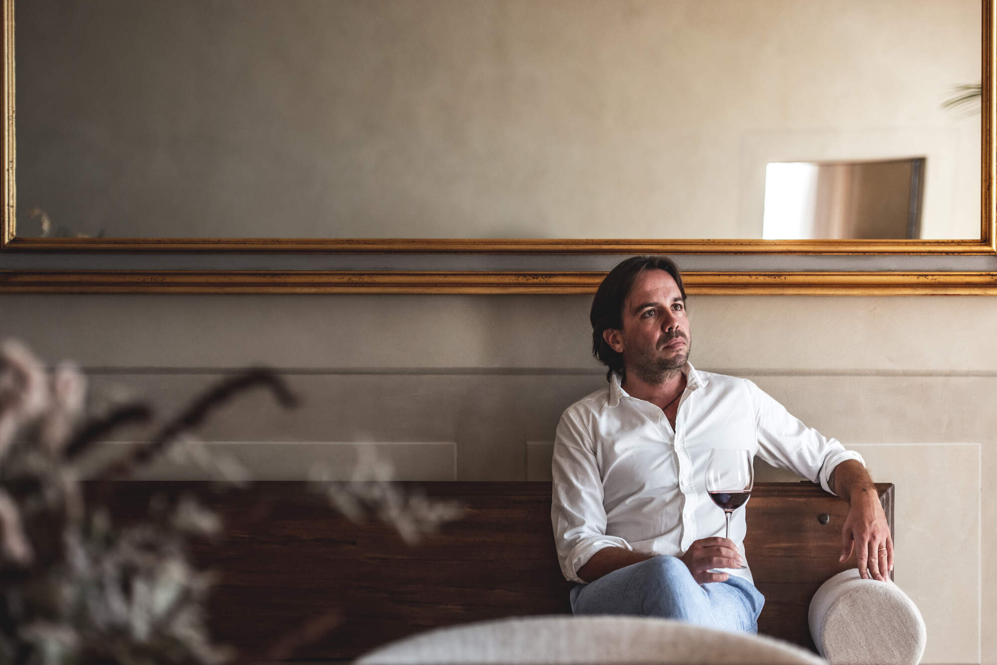 Man sitting on a wooden bench holding a glass of red wine.