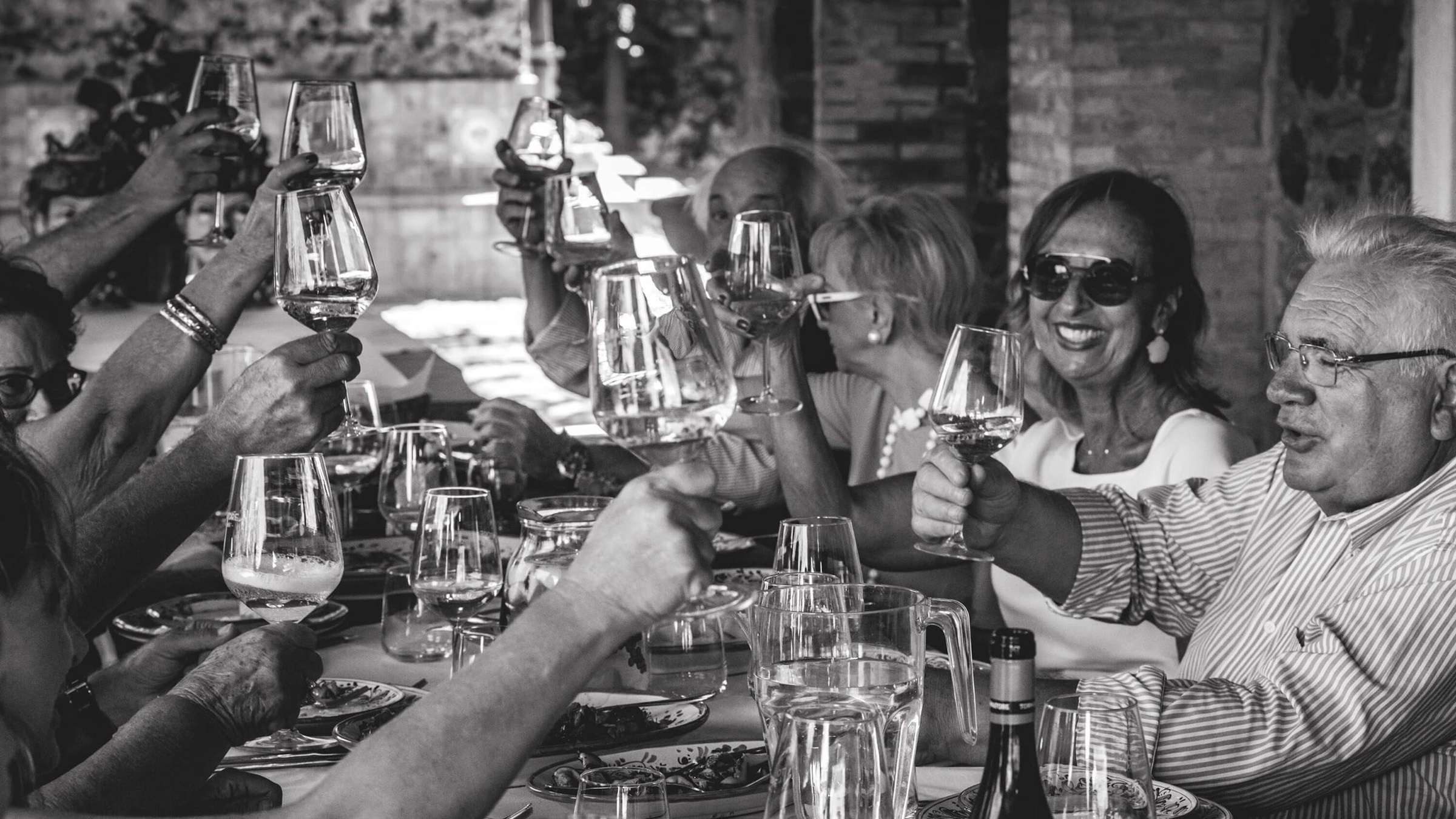 A group of people gathered around a dining table with wine glasses raised to toast.
