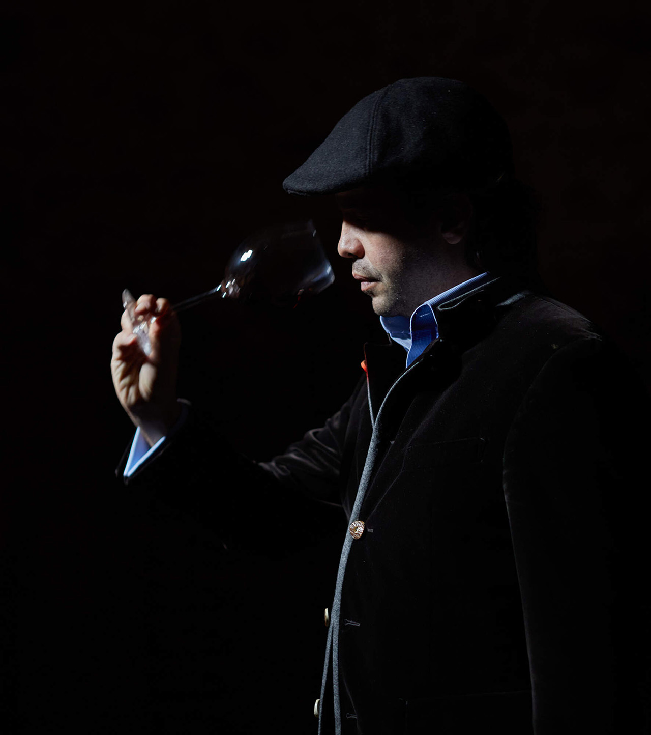 man standing against a black background sampling wine.