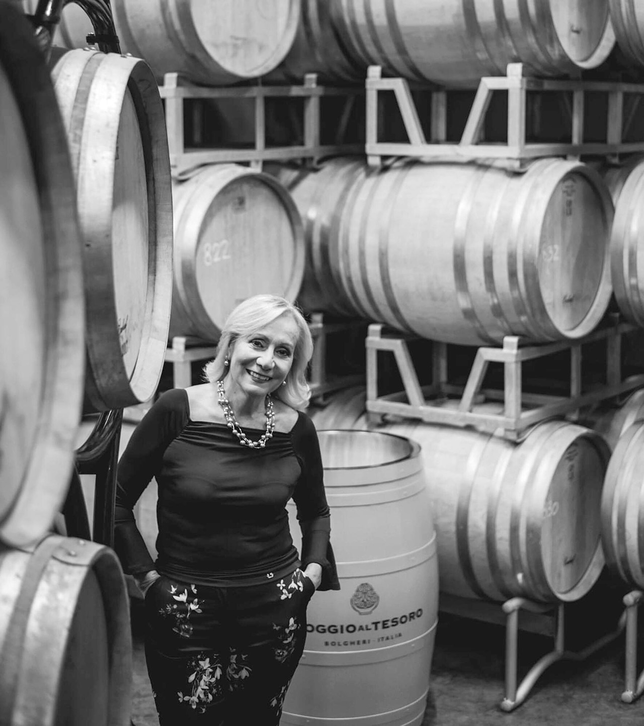 Black and white image of lady standing in a wine cellar with her hands in her pant pockets.