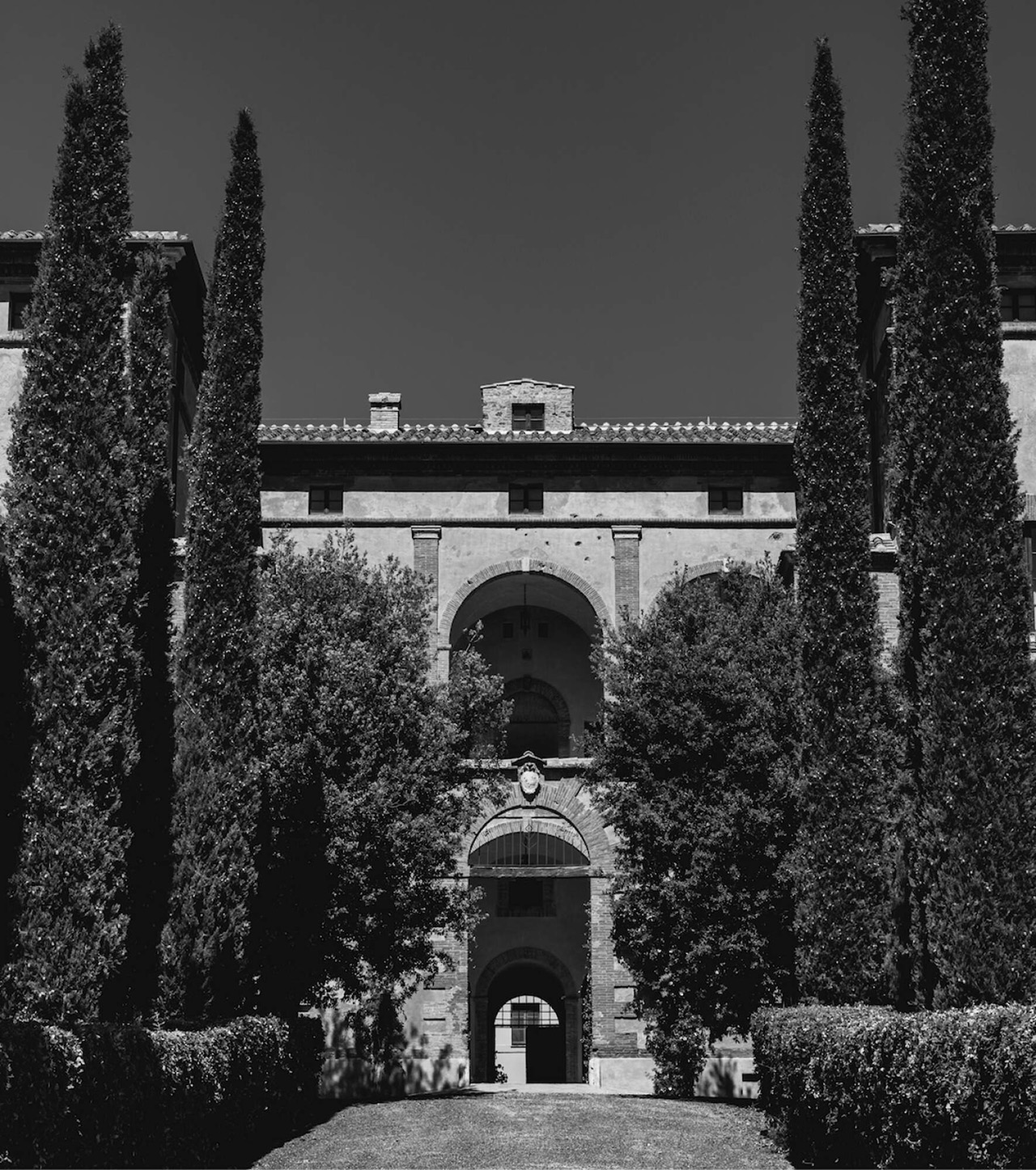 Front view of an historic building flanked either side with tall evergreen trees 