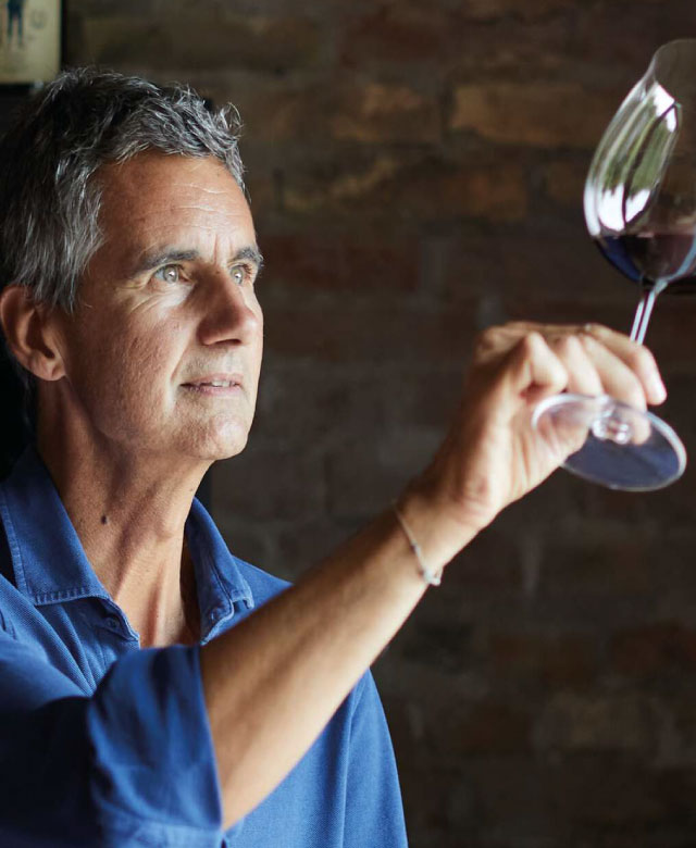 Man holding up a glass of red wine to the light.