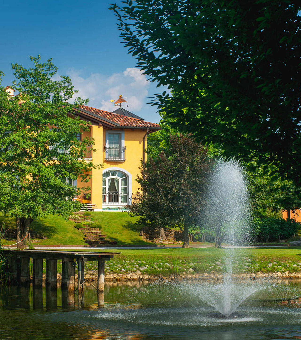 Lake with fountain outside a vibrant yellow Italian villa.