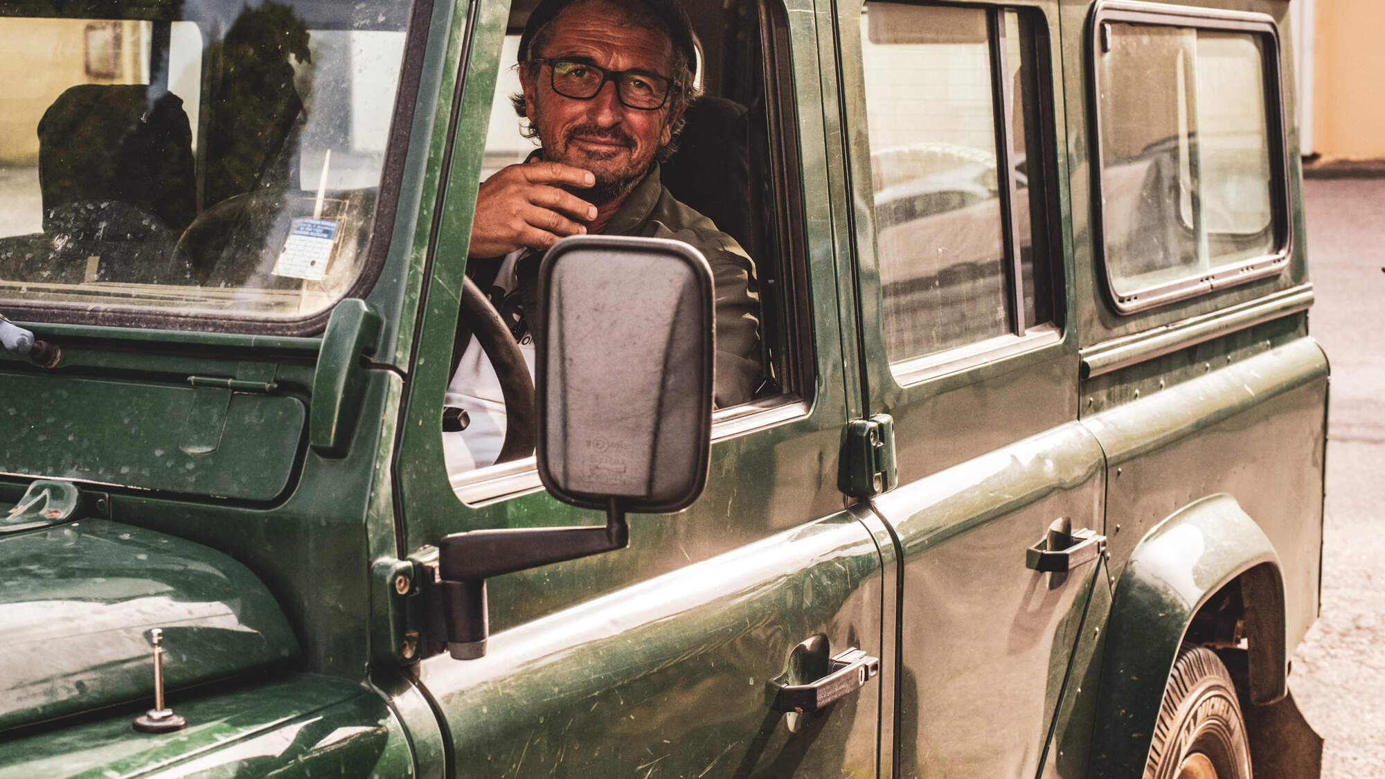 Man wearing glasses sitting in a jeep, looking out of the drivers seat window.
