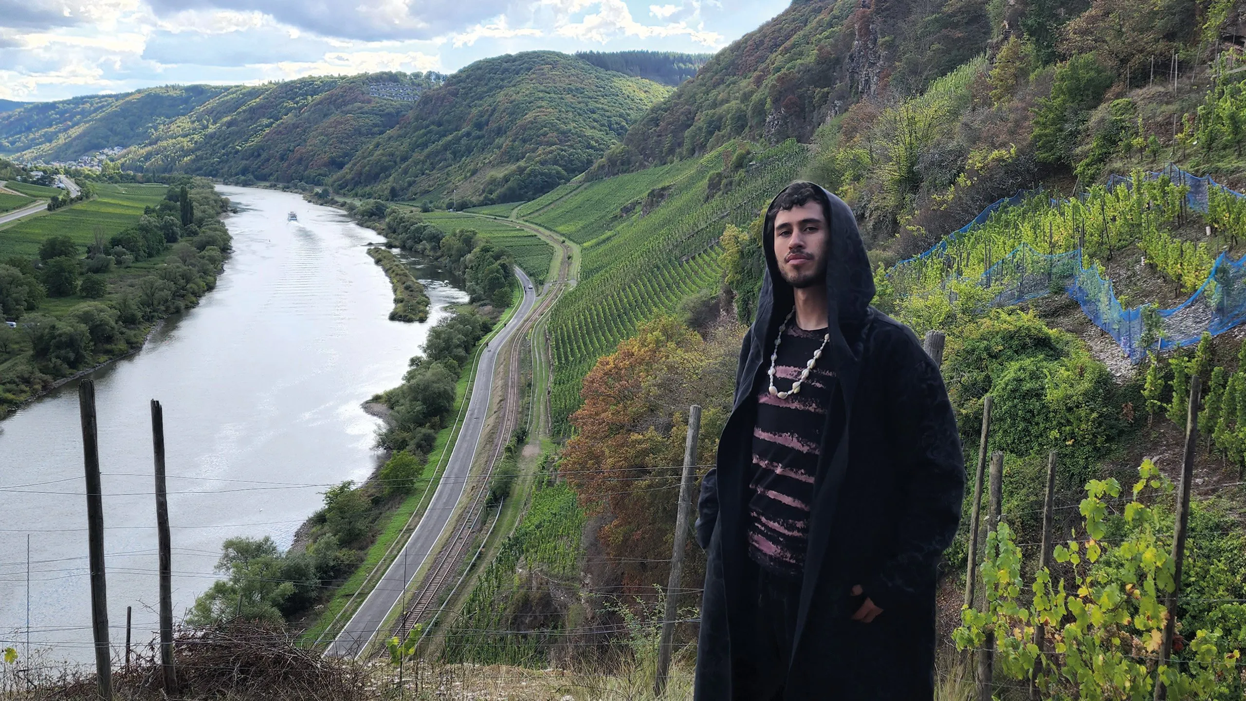 Person standing among hillside vineyards overlooking a winding river and valley.