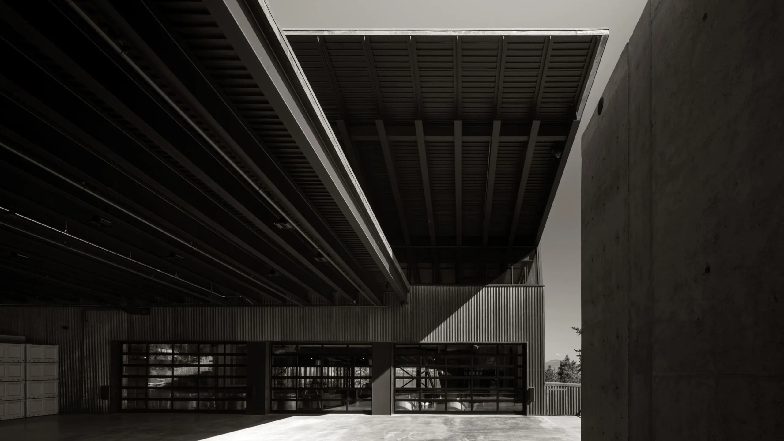 Modern industrial building with dramatic steel roof structures, concrete walls, and large glass garage doors.