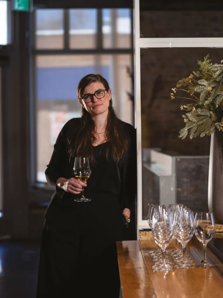 Woman holding a glass of wine beside a table lined with empty wine glasses.