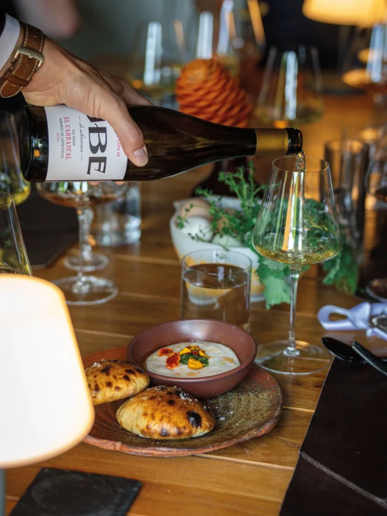 White wine being poured into a glass beside a plated appetizer on a restaurant table.