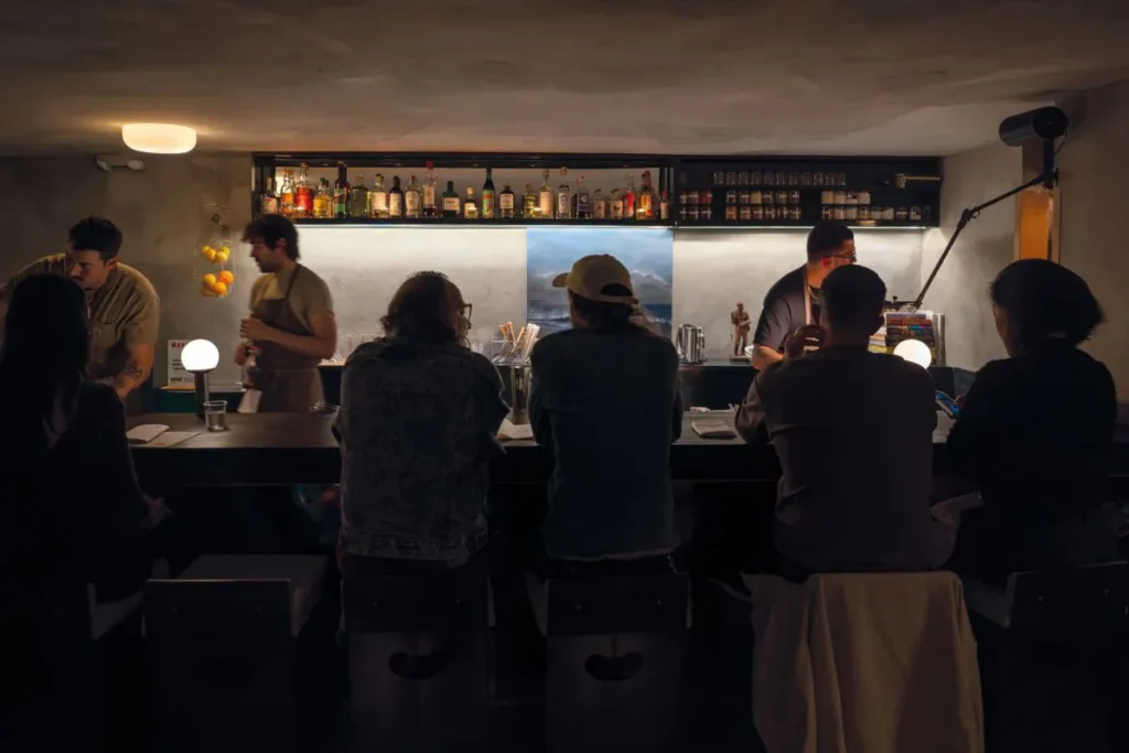 Guests seated at a dimly lit restaurant bar while bartenders work behind the counter.