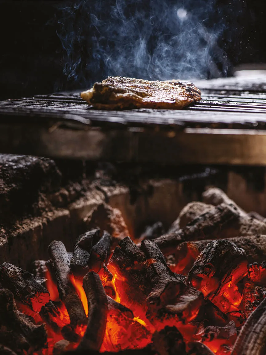 Meat searing on a grill over glowing charcoal