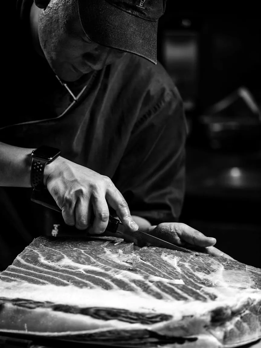 Chef slicing a side of tuna in black and white