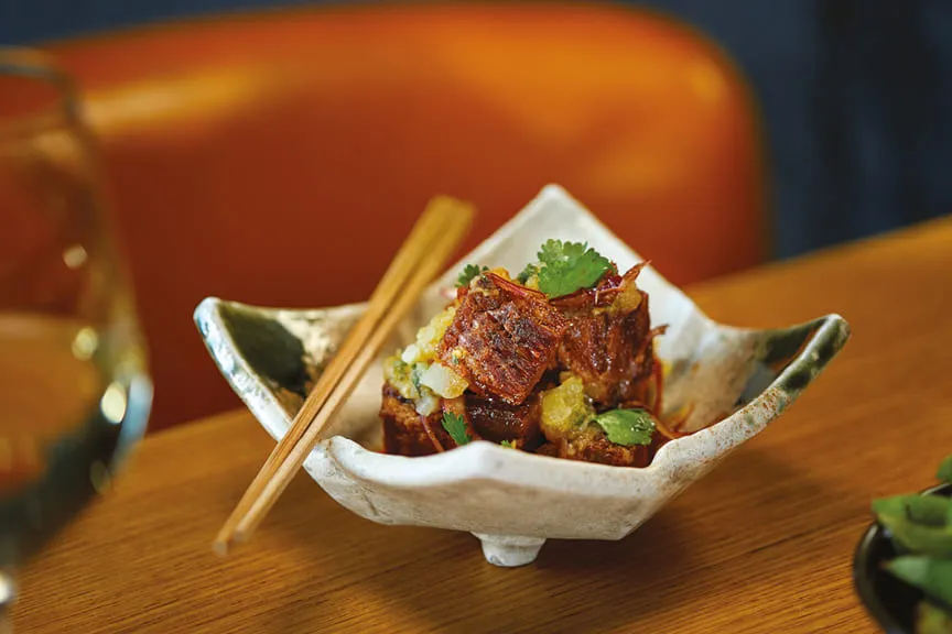 Crispy meat dish garnished with herbs and sauce, served in a ceramic bowl with chopsticks.