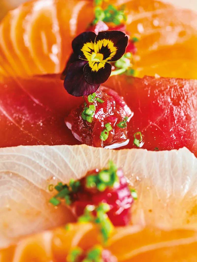 Colorful sashimi slices garnished with green onions, sauce, and an edible flower.