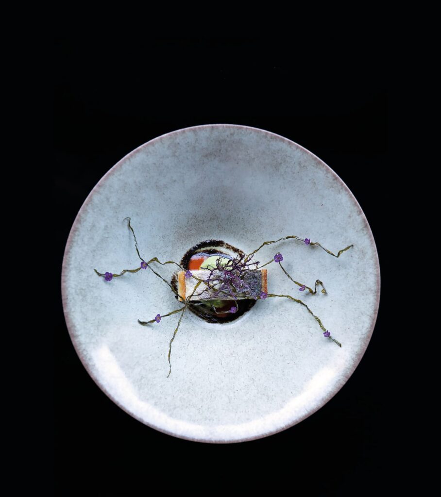 Artistic fine-dining dish delicately garnished with herbs and small purple flowers on a white plate.