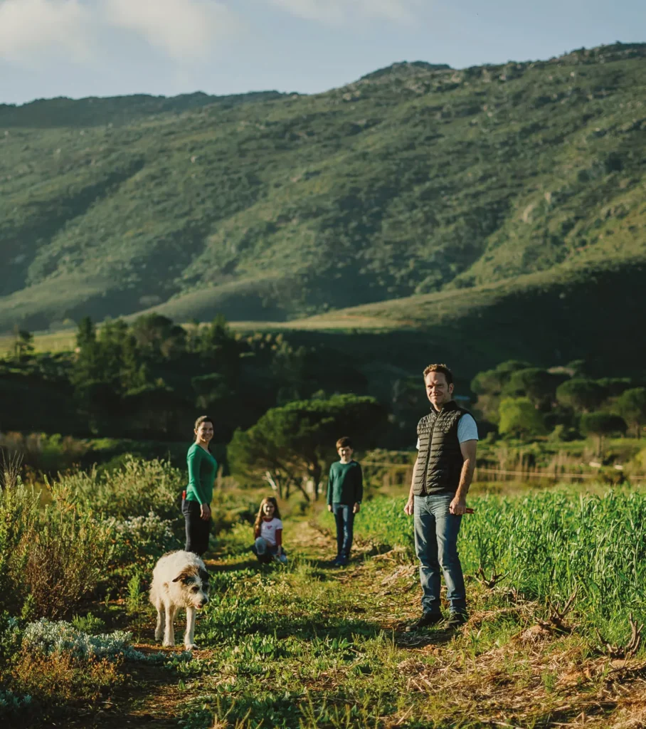 Family with a dog standing among green crops in a scenic mountain valley.
