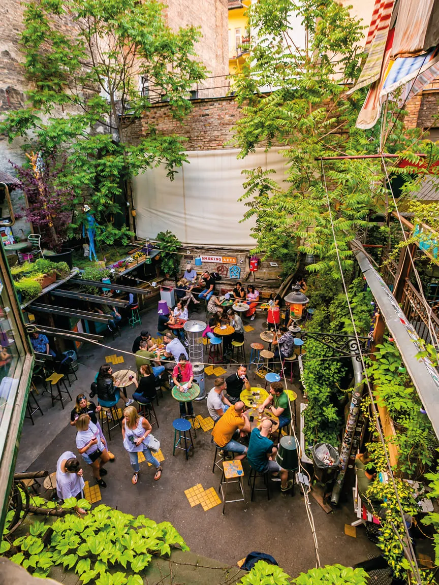 Overhead view of a lively outdoor café courtyard filled with people, colorful tables, and lush greenery.