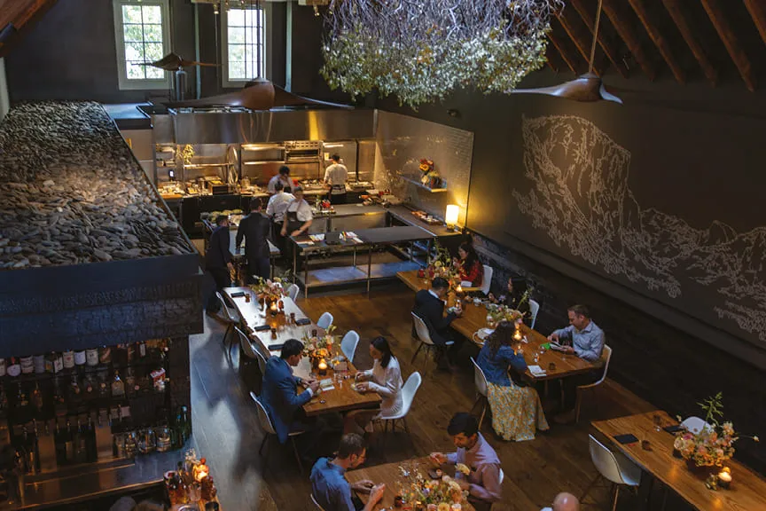 Dining room with guests and an open restaurant kitchen.