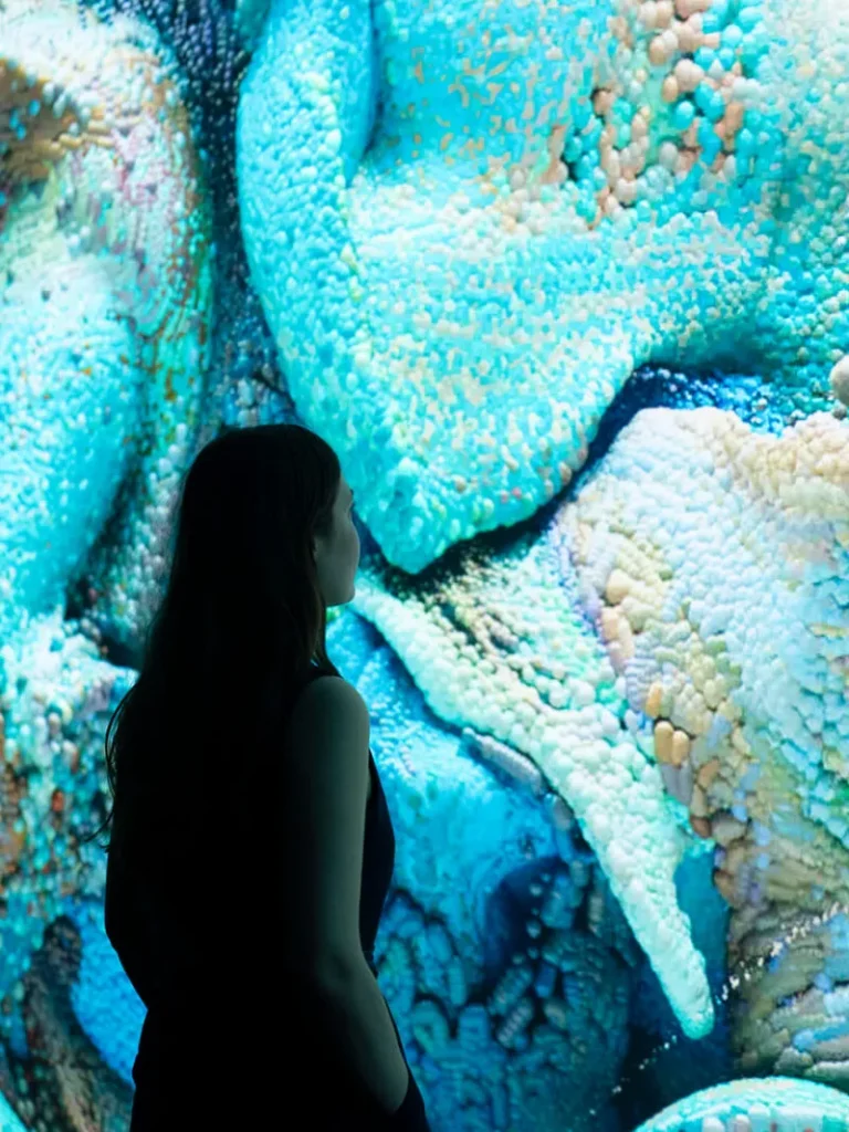 Woman viewing a large immersive digital art installation featuring vibrant blue and turquoise abstract textures.