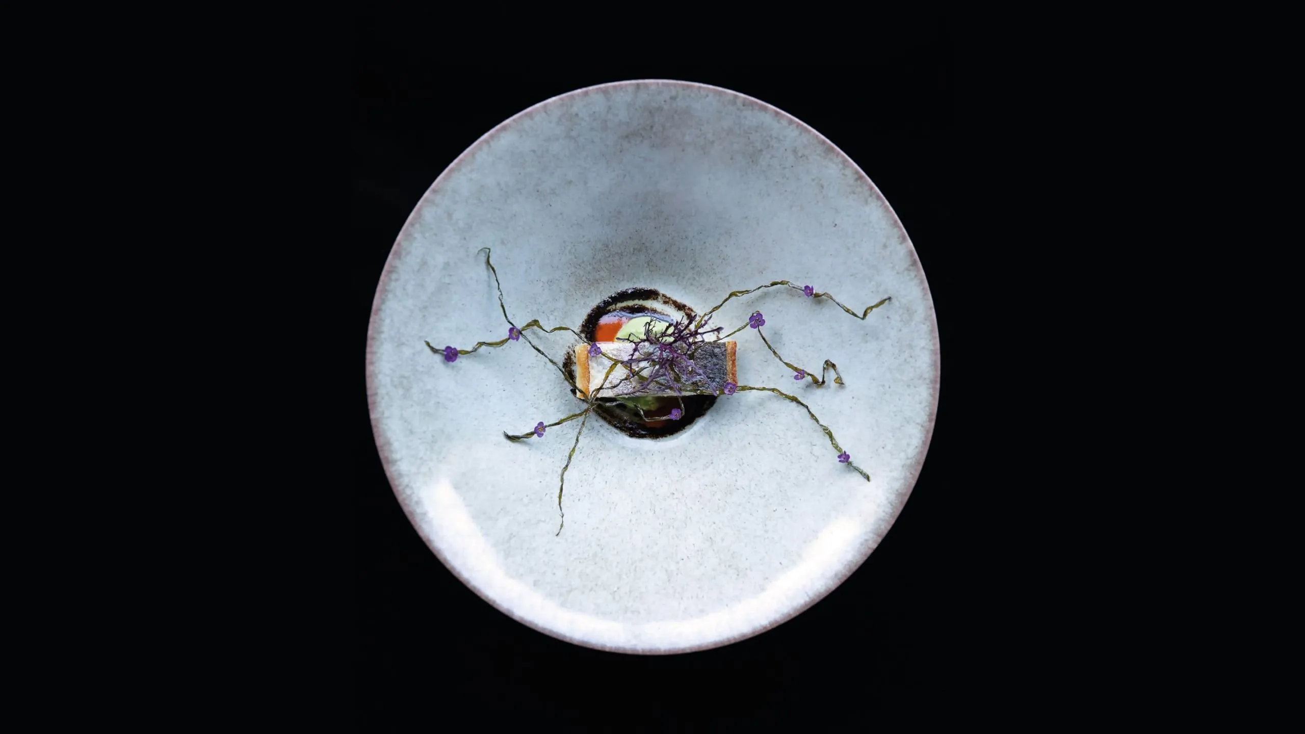 Artistic fine-dining dish delicately garnished with herbs and small purple flowers on a white plate.