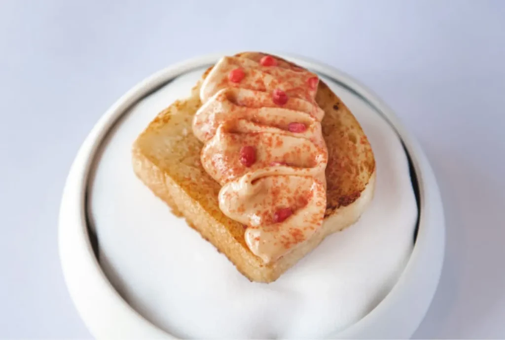 Small toasted pastry topped with piped cream and pink garnish on a white plate.