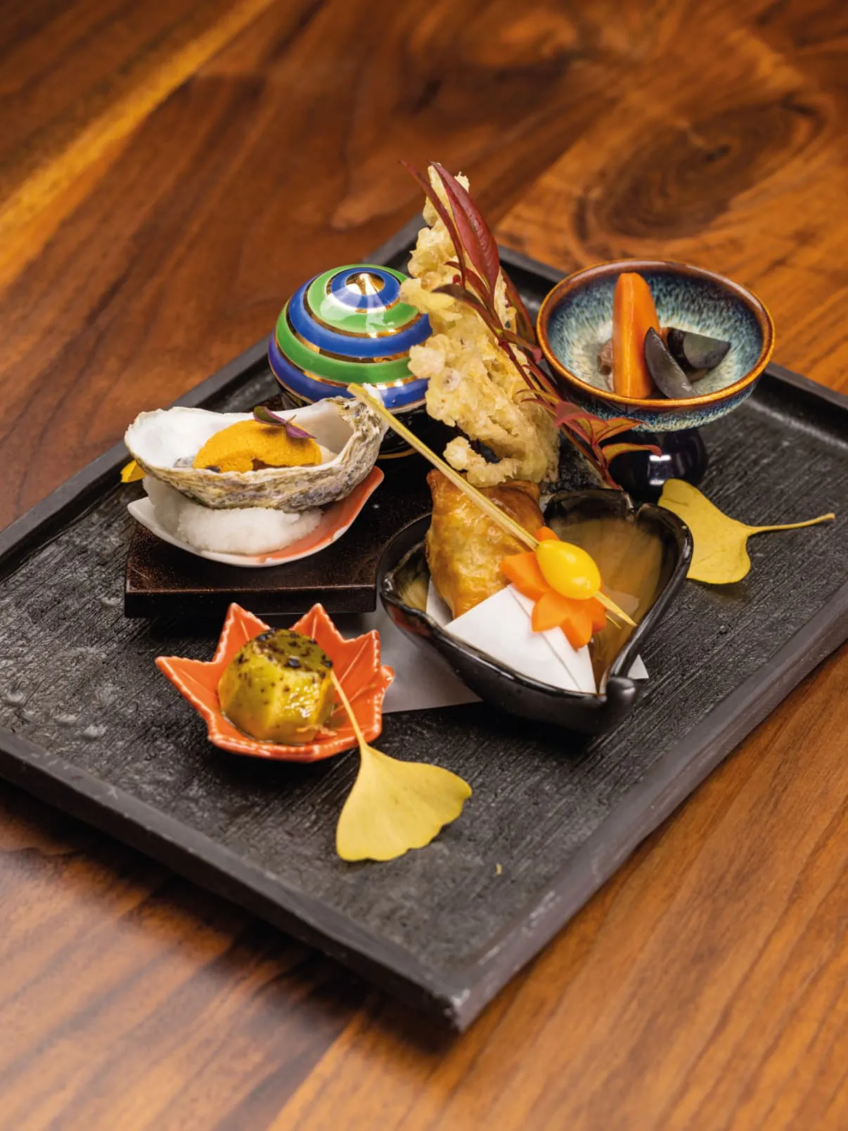 Assortment of Japanese dishes, including tempura and seafood, arranged on a black serving tray.